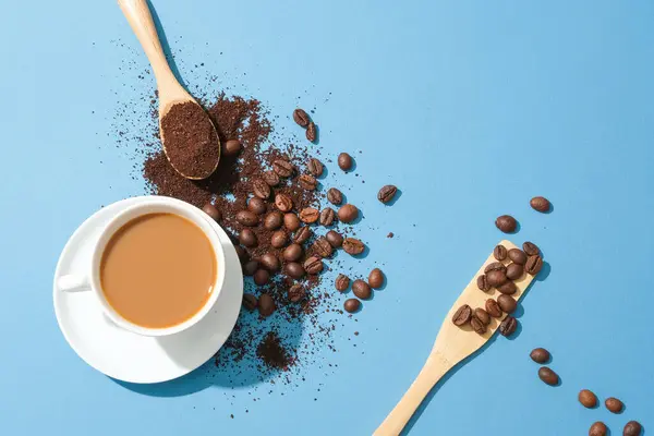 A glass of milky coffee is placed next to coffee beans and coffee powder on a blue background. Coffee helps block chemicals that cause muscle fatigue during intense physical activities.