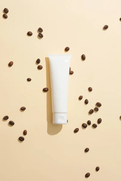 咖啡豆分散在浅粉色的背景上 有一个没有标签的化妆品管 用咖啡粉按摩能增加皮肤的弹性和坚韧度 — 图库照片