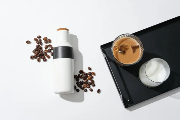 On the black tray there is a cup of milk and a cup of milk coffee, a thermos and coffee beans on a white background. Caffeine helps the body restore muscle strength and improve exercise performance.