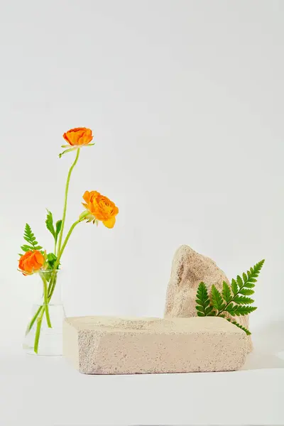 オレンジ色の花は 白い背景にある石のプラットフォームの横にあるエレクトライヤーフラスコに置かれています プロダクト表示のための理想的なスペース フラワーコンセプト — ストック写真