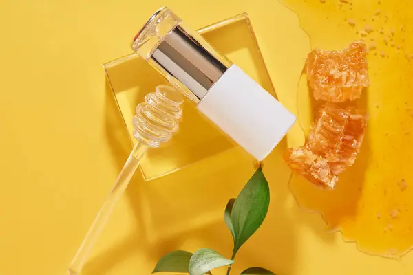 Cosmetic bottle decorated with a honey dripping on glass podium. Honey and beeswax featured on yellow background. Branding mockup of Honey extract