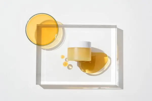 透明なガラスプラットフォームにハチミツの滴が付いているブランド化粧品の瓶のクローズアップ 蜂蜜は非常によい皮の保湿剤として使用されます — ストック写真