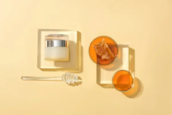 一罐未加品牌的化妆品放在一个玻璃平台上 两个装有蜂蜜和蜂蜜毛毛雨的培养皿放在米色背景上 具有理想空间的化妆品广告 — 图库照片