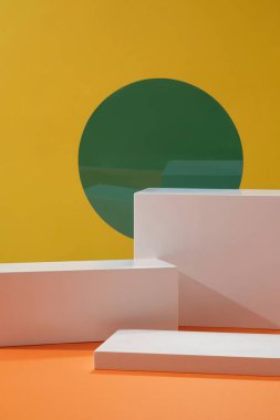Silindir beyaz podyumlar ve sarı zemin üzerine dekore edilmiş yuvarlak yeşil akrilik çarşaf ile boş bir vitrin şablonu. Kozmetik ürün sunumu için alan.