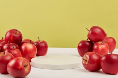 Yeşil arka planda, olgun kırmızı elmalar yuvarlak beyaz bir podyumun etrafında. Doğal özlü kozmetik ürününün sunumu için alan - kırmızı elma.