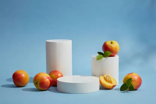 Minimal empty display product presentation scene with peach. Cylinder white podiums displayed on blue background with fresh peaches. Peaches are very nutritious and can provide many health benefits