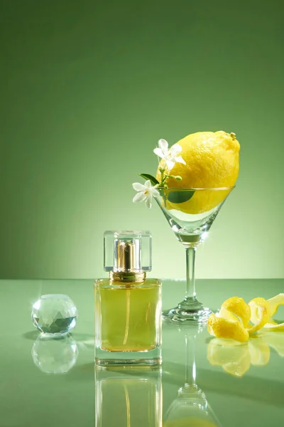 Scene for advertising fragrance oil products from lemon oil. Perfume bottle prototype unlabeled with glass cup containing lemon and white flower, crystal ball and peel of lemon on green background