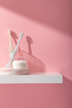 Ağız bakımı için reklam sahnesi ve cam bardakta diş fırçası olan temizlik ürünleri ve kaidedeki, pembe arkaplandaki makyaj pamuğunu çıkarmak. Metin ve tasarım için boşluk.