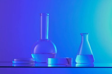 Mavi zemin üzerinde renksiz sıvı ve şeffaf podyum bulunan laboratuvar camlarının ön görüntüsü. Laboratuvar konsepti ile kozmetik ürün sunumu için kaldırım taşı.