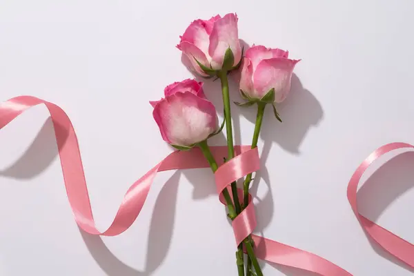 精致的玫瑰包裹在白色背景上柔软的粉红色缎带上 广告化妆品或设计卡片 明信片和横幅时 平铺着美丽花朵的构图 — 图库照片