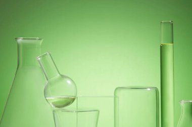 Yeşil arka planda süslenmiş sarı sıvı içeren laboratuvar camlarının önü. Ekran ürünü için boş alan. Doğal özü olan kozmetik ürünleri araştırma ve geliştirme kavramı