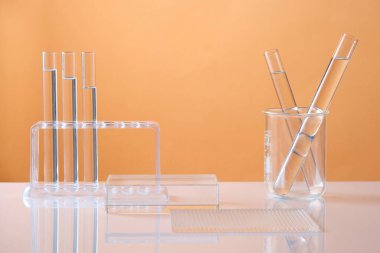 Renkli arka planda renksiz sıvı içeren şeffaf podyum ve laboratuvar camlarının ön görüntüsü. Asgari konsepte sahip kozmetik ürünü göstermek için boş alan.