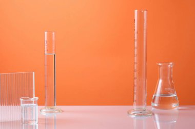 Renksiz sıvı ve turuncu neon arka planda tırtıklı akrilik çarşaf içeren laboratuvar ekipmanları ile boş minimal konsept. Kozmetik ürün sunumu için ortada boş alan