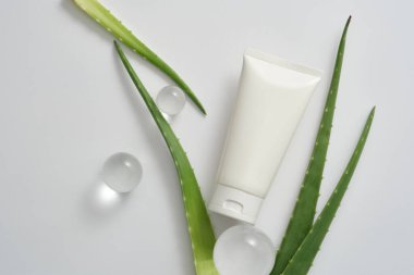 Markalaştırma için boş arkaplan ve minimal sunum - beyaz arka planda süslenmiş cam toplar ve taze aloe vera yapraklarıyla damgalanmamış beyaz plastik şişe. Tasarım için alan. Üst görünüm