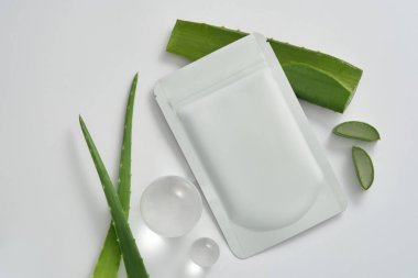 Yüzü aloe vera maske paketiyle markalaştırma ve paketleme modeli, beyaz arka planda aloe vera yaprakları ve cam toplar. Aloe vera tabanlı güzellik ürünü paketleme tasarım şablonları