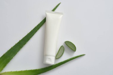 Temizleyici veya nemlendirici için beyaz, boş plastik kozmetik kabı, beyaz arka planda taze aloe vera yaprakları ve dilimler. Doğal özün kozmetik ürünü Aloe Barbadensis için model.
