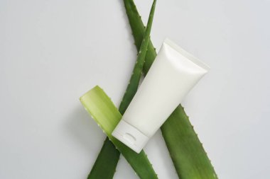 Taze aloe vera yapraklı beyaz arka planda yüz bakımı için doğal aloe özütüyle yenilenen ve nemlendirici kozmetikler. Etiketsiz beyaz plastik tüplü maket sahnesi.
