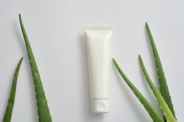 Yüz nemlendirici kremiyle etiketlenmemiş beyaz plastik tüp ya da beyaz arka planda taze aloe vera yapraklı yüz temizleyici. Aloe vera içeriğinden kozmetik reklamı sahnesi. Boşluğu kopyala