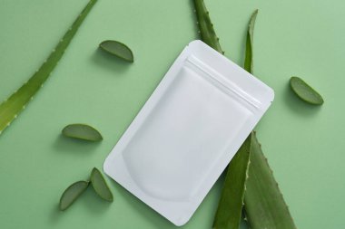 Aloe vera (Aloe barbadensis) ve yeşil arka planda bir çarşaf maskesi. Maske olarak Aloe vera özünün birçok deri etkisi vardır: nemlendirici, beyazlatıcı, yatıştırıcı ve yaşlanmayı önleyici.