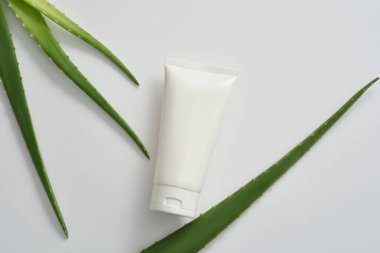 Beyaz plastik tüp etiketsiz aloe vera malzemesi ve beyaz arka planda süslenmiş taze aloe vera yapraklı kozmetik, temizleyici ya da nemlendirici ürünler için taklit sahnesi. Tasarım için boşluk.