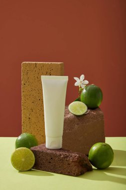 Limon özünün kozmetik ürünü olarak etiketlenmemiş boş şişeyle taklit sahnesi. Taze limon ve arka planda koyu renkli taşlara yerleştirilmiş küçük beyaz çiçek. Ön görünüm, tasarım için alan