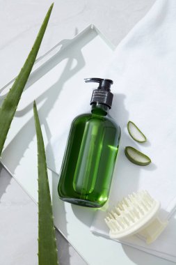 Yeşil etiketsiz şampuan ürünü, tarak, havlu ve beyaz arka planda taze aloe vera. Aloe Vera birçok amino asit ve proteolitik enzimler içerir. Bu vitamin saçlara iyi gelir.