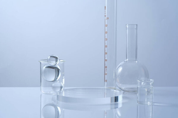 An empty transparent podium, glass balls and lab glassware decorated on white background. Minimal background with copy space for cosmetics and product presentation. Laboratory concept
