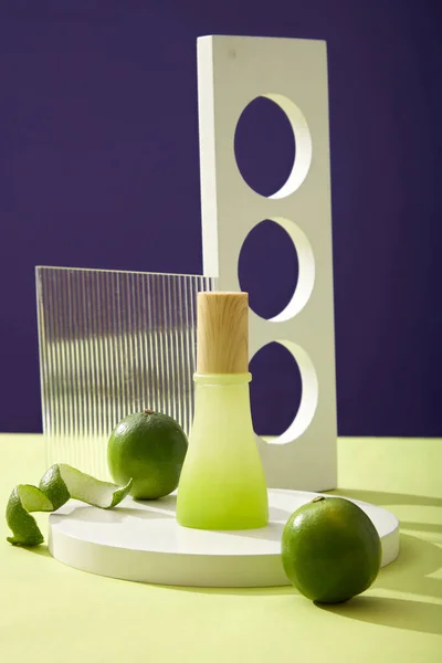 石灰提取物产品的模型场景 圆形讲台上的玻璃瓶 几何对象和新鲜石灰柑橘 螺旋形石灰皮装饰紫色背景 设计空间 — 图库照片