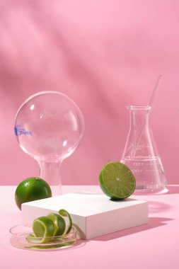 Laboratuvar konseptli reklam ürünü sahnesi. Taze limon ve pembe arka planda labaratuvar camlarıyla süslenmiş kabuk. Beyaz boş podyum sunum için limondan malzemeyle kozmetik