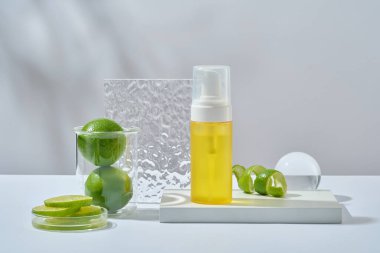 Beyaz podyumda etiketsiz sarı şişe, beher ve petri kabında taze limon, beyaz arka planda akrilik çarşaf ve cam top. Limondan elde edilen kozmetik ürün modeli