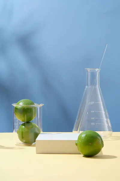 Świeże Limonki Niebieskim Tle Szklaną Zastawą Laboratoryjną Białym Pustym Podium — Zdjęcie stockowe
