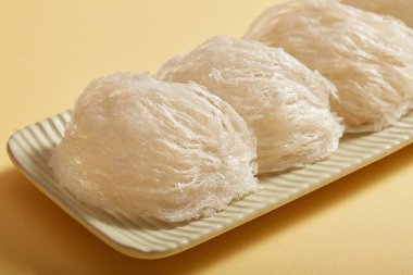 Bazı ham kuşların yuvalarının yakınları bej arka planda beyaz, uzun dikdörtgen bir plakaya yerleştirilmiştir. Doğal kaynaklı yiyecekler, sağlık için pahalı mutfak malzemeleri..