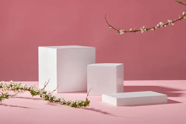 3つの白い空の表彰台とピンクの背景にある白い花の枝 化粧品や製品プレゼンテーション用のコピースペースを備えた最小限のアートバック フロントビュー — ストック写真
