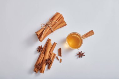 Tarçın çubukları, anason ve beyaz arka planda gerekli yağları içeren küçük bardakların üst görüntüsü. Doğal bitkisel özün kozmetik veya ürünü için minimum doğa sahnesi.