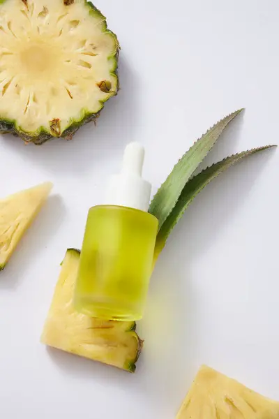 一个没有标签的玻璃瓶 装有黄色液体 有水滴盖 新鲜的菠萝片和白色背景的叶子 用于血清产品的调理 来自天然提取物 顶部视图 — 图库照片