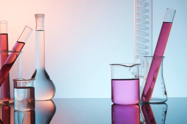 Laboratuvar ekipmanlarının ön görüntüsü - deney tüpü, deney tüpü ve mor renkli arka planda kaynayan matara dolu sıvı. Konsept: araştırma, biyokimya, doğa, ilaç