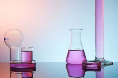 Laboratuvar temalı laboratuvar teması - Erlenmeyer şişesi, test tüpü, petri kabı ve mor arka planda kaynayan şişe. Ürün ve metin görüntülemek için boşluk.