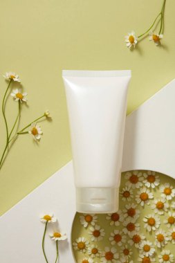 Beyaz podyumda beyaz boş plastik şişe ve açık yeşil zemin üzerinde taze ateş (tanasetum partenyum). Kozmetik için doğal bir taklit sahnesi. Asgari konsept.