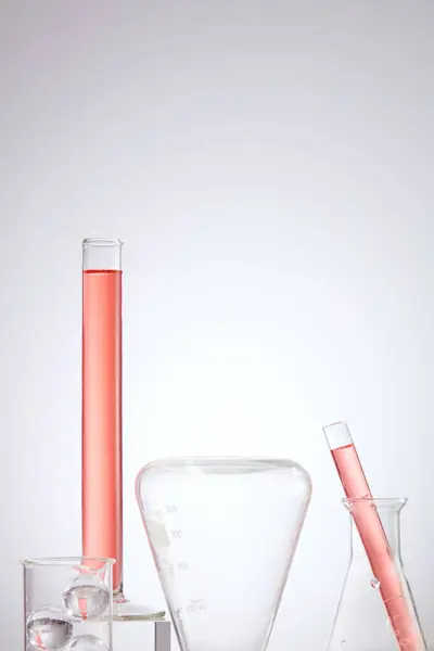 Laboratory concept with lab glassware containing pink liquid on light background. Lab theme. Science and medical background, front view.