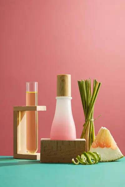 Mockup scene of pink glass bottle containing cosmetics products with pink pomelo and lemongrass essential oils on pink background. Test tube containing pink pomelo essence placed on a wooden stand.