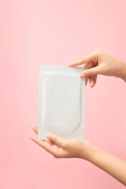 Pastel pembe arka planda maske takan güzel kadın elleri. Yüz güzelliği için kozmetik ürünler için reklam sahnesi, yaşlanma karşıtı, temizlik önleyici, nemlendirici kompleks