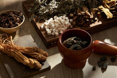 Ahşap tepsi, podyum, kase, havan topuzu ve ahşap masa arkasındaki geleneksel otların en üst görüntüsü. Tonik hazırlamak için bitki koleksiyonu