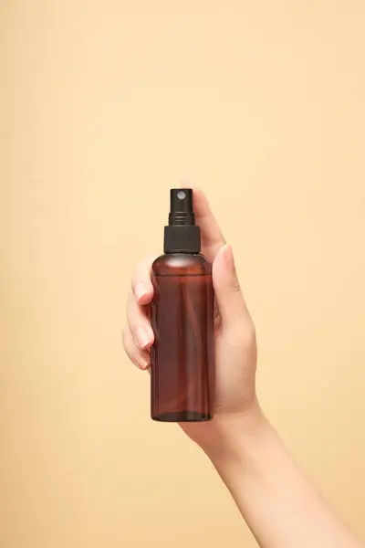 Front view of an amber bottle empty label on female hand, on beige background. Mockup scene for advertising cosmetic product of bottle spray. Copy space, blank for design.