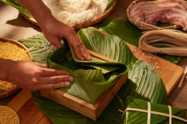Ahşap mutfak arka planında domuz pirinçli ve mısırlı Chung cake (yapışkan pirinç keki) yapan şefin ön görüntüsü. Çin Yeni Yıl Kutlaması