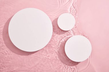 Üç beyaz dairesel boş podyumun üst görüntüsü, su ve küçük dalgalarla pembe bir zemin üzerine kurulmuş. Sergi ürünleri için boş alan. Boş asgari tasarım kavramı.