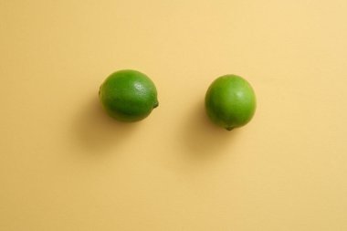 Bej bir arka planda, iki limon izole edilir. Lime 'dan (Citrus aurantiifolia) elde edilen güzellik ürünlerini göstermek için boş alan. Boşluğu kopyala