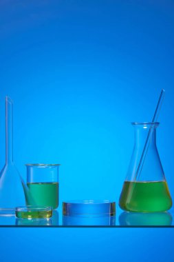Erlenmeyer matarası, petri kabı ve mavi arka planda sarı sıvıyla dolu bir deney şişesi. Reklam için boş yuvarlak şeffaf kaide