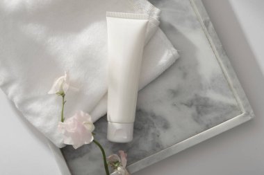 Havlu ve mermer tepside beyaz çiçek dalıyla düzenlenmiş boş etiketli beyaz bir tüp. Cilt bakımı markalaşmasının konteyner paketi