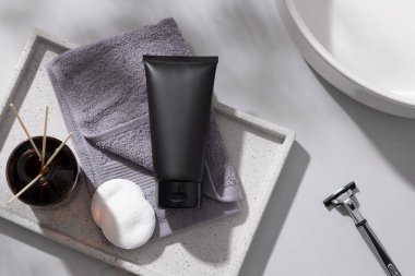 Dikdörtgen tepside gri bir havlu, siyah bir tüp, pamuk pedleri ve kamış ayırıcıları, yanında da tıraş ve yıkama leğeni. Cilt Temizleme Ürün Model