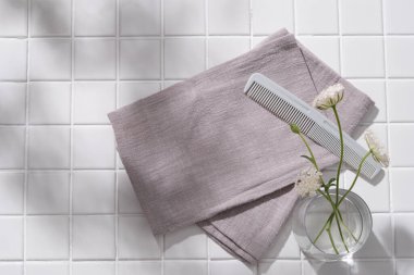 Cam vazo, fırça ve gri havlular ile bembeyaz seramik zemin üzerinde düz çiçek yatıyordu. Banyo manzaralı güzellik ürünleri konsepti